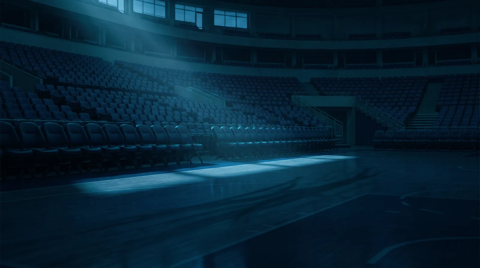 An empty professional basketball arena at dusk, rows of vacant seats and a shaft of cool light across a shadowed court, in deep teal and navy tones.
